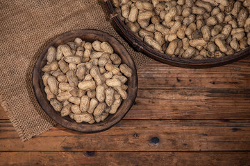The container on the wood grain table is full of peanuts