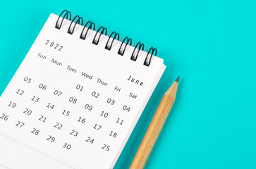 June 2022 desk calendar with wooden pencil on light blue background.