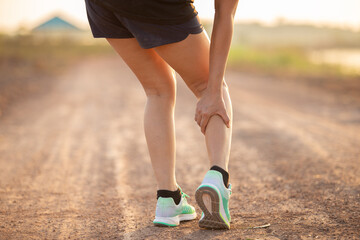 injury concept from exercise : Asian woman hands on thigh while running on park road. Shot in the morning, sunlight and warm effects.