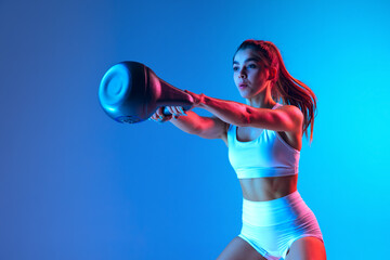 Young sportive girl training with sports equipment isolated on gradient blue-pink studio background...