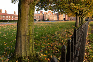 Tudor facade and main entrance to Hampton Court Palace seen through plane trees that line the footpath next to the river Thames