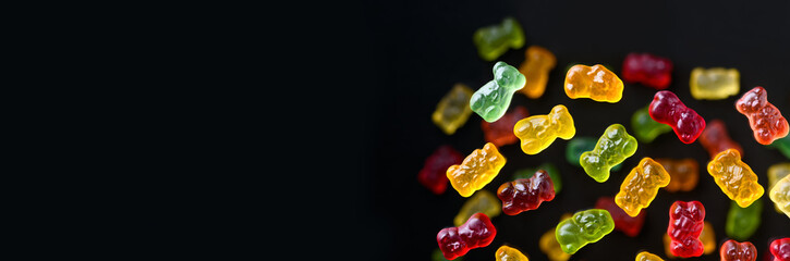 Multicolored flying gummy bears on a black background, flat lay. Banner