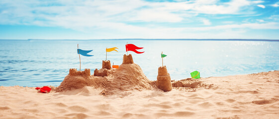 Sand castle with colourful flags on the beach of the sea - obrazy, fototapety, plakaty