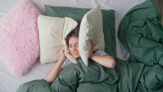 A Young Woman in Bed Tries To Rest, Irritated By Noisy Neighbors. Insomnia, Thin Walls of the House, Apartment Without Sound Insulation, Repair Work at the Neighbors. The Concept of Neighborhood.