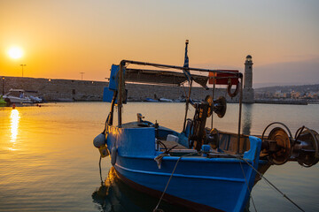 Fototapeta na wymiar Scenic shot of a calm fisher boat with a scenic sunrise at the greek harbor of Rethymno old town in Crete, Greece