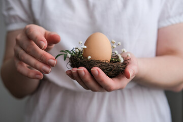 Nest with an egg in female hands. Natural eco-friendly Easter decor. Easter decor in rustic style