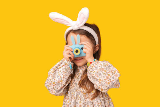 Cute kid girl is holding a small camera and taking a shot in a studio.