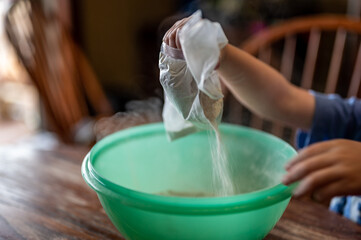 Little child dumping ingredients into a bowl causing dust to rise into the air.