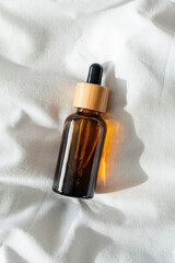 Amber glass bottles with dropper pipette with serum or essential oil on light fabric background.