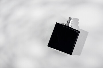 Black bottle of perfume on a white background. Fragrance presentation with daylight.