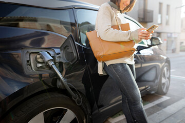 Cropped Woman using smartphone while waits for electric car to charge.