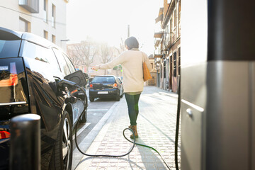 Woman walking away after plug the electric car to the city charging station.