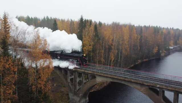 Steam locomotive with smoke from a chimney on a bridge over a river in Karelia