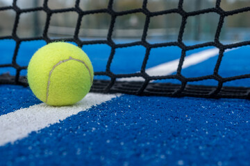 Yellow ball on floor behind paddle net in blue court outdoors. Padel tennis