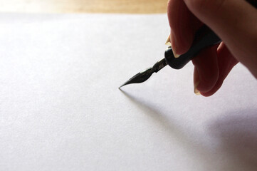 female hand holding a black fountain pen on white paper with copy space