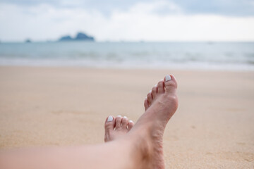 Closeup image of a female's legs and feet while sitting by the sea with blue sky background