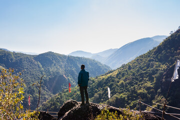 isolated young man at mountain top with green forests and misty blue sky at morning from flat angle