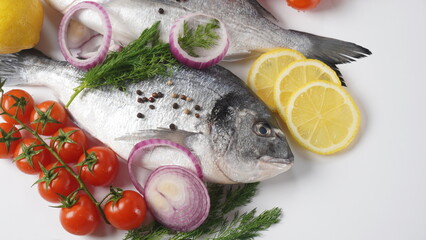 Raw fresh uncooked dorado or sea bream fish with lemon, herbs,  cherry tomatoes and spices on  black background