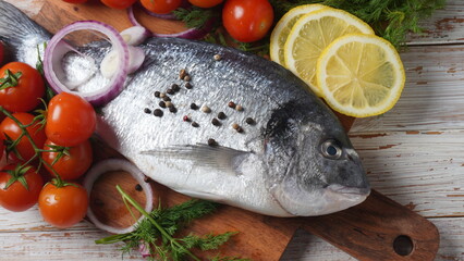 Raw fresh uncooked dorado or sea bream fish with lemon, herbs,  cherry tomatoes and spices on  black background