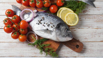 Raw fresh uncooked dorado or sea bream fish with lemon, herbs,  cherry tomatoes and spices on  black background