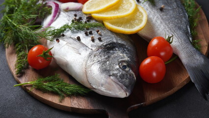 Raw fresh uncooked dorado or sea bream fish with lemon, herbs,  cherry tomatoes and spices on  black background