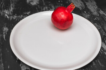 Red pomegranate on big white plate on black and white wooden background. Garnet is a symbol of Judaism.