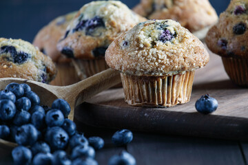 Rustic image of homemade blueberry muffins with fresh berries falling from a wooden spoon. Selective focus with extreme blurred foreground and background.