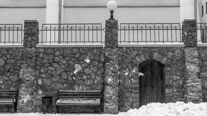 Black and white image of wooden benches with snow and ice. The seating area is directly in front of a stone wall.