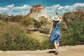 A young woman tourist stands in front of the Pyramid of the Magician in an ancient Mayan complex Uxmal in Mexico. The girl enjoys the view of the Mayan pyramid. Travel concept