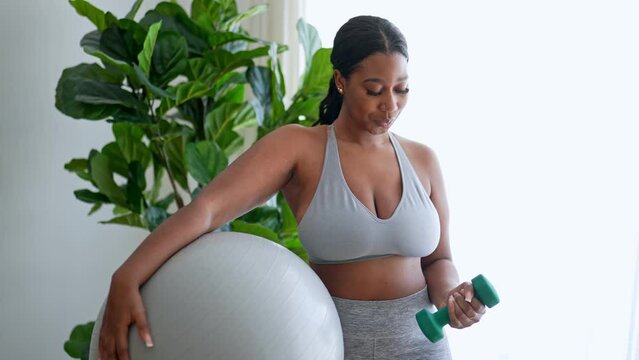 African american woman working out in home living room gym with training ball