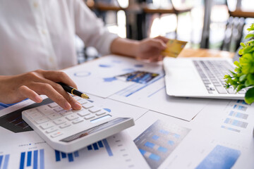 Businesswoman working at her desk using calculator to calculate earnings figures, profit, calculate monthly expenses, taxes, manage budget accounting concepts.
