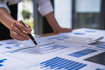 Businesswoman holding graph pen to analyze marketing plan, turnover and profit, calculating taxes with calculator and laptop on wooden desk in office.