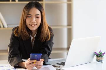 Business woman in office working with laptop using mobile phone on desk.