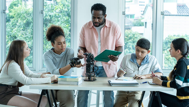 group of international students of Asian, African American youths and white girls sit and study with educational robot hands guided by teachers in school classrooms.