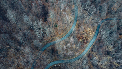 Aerial high angle view of narrow winding curvy mountain road among the trees in winter forest. Bird's eye view landscape.