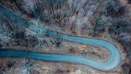 Aerial high angle view of narrow winding curvy mountain road among the trees in winter forest. Bird's eye view landscape.