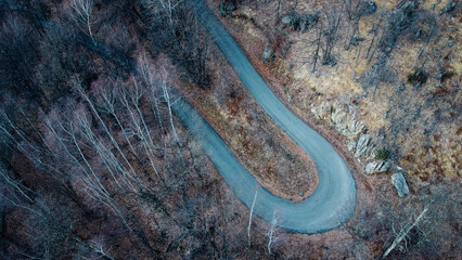 Aerial high angle view of narrow winding curvy mountain road among the trees in winter forest. Bird's eye view landscape.