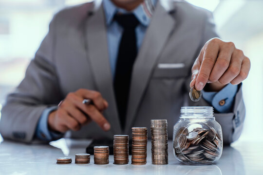 Asian businessman holding coins in a piggy bank to collect money About Finance Accounting Income Tax and Accounting while the concept of maximizing profit from business investments, saving money