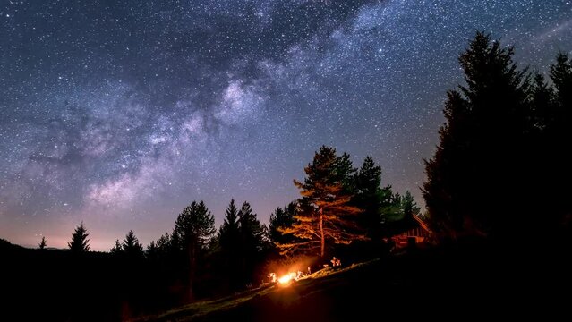 Bunch of friends sitting over campfire in summer nature forest under magic milky way galaxy stars Astronomy Space Time lapse