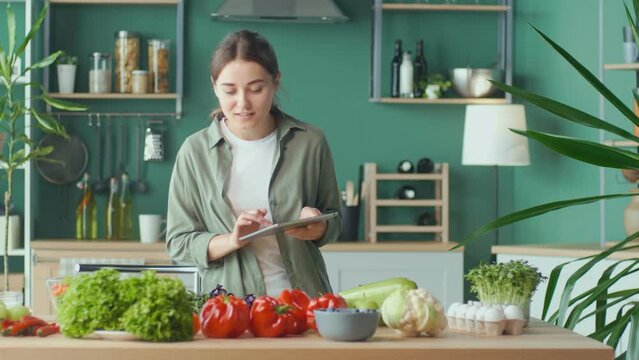 Young Woman Makes a Diet Plan of Correct Nutrition Using a Tablet in the Kitchen, Using a Calorie Counter in a Weight Loss App. Nutrition and Dietetics. Healthy Food and Technology Concept.
