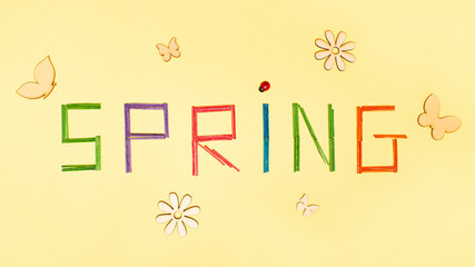 Spring letters on bright yellow background decorated with butterfly, flowers, ladybug, colorful letter. Spring is coming, minimal  flat lay concept.