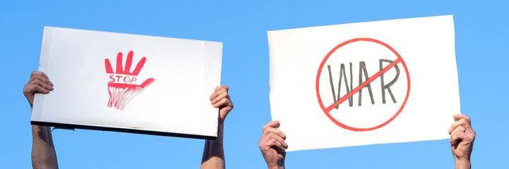 banner with two pairs of people's hands with homemade posters against war against the blue sky