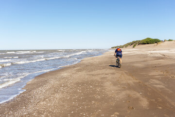 Unrecognizable person riding a bike on the beach. Ample copyspace.