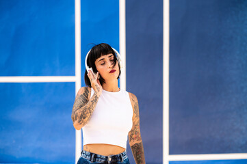 Una mujer caucásica con tatuajes y pelo corto escuchando música con unos auriculares en una pista...