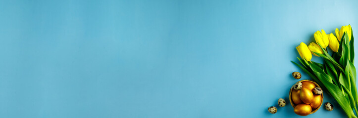 Easter golden and quail eggs and yellow tulips flat lay blue background copy space for text. Modern painted wooden easter eggs and spring flowers. Greeting card template, beautiful easter background