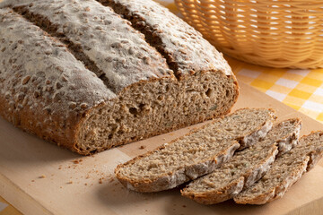 Loaf of Pavé bread, multi grain bread,  and slices close up on a wooden cutting board  