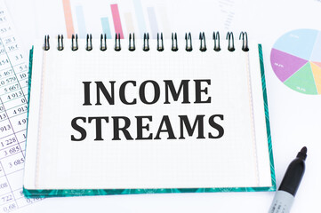 INCOME STREAMS text is written on a notebook against the background of charts and financial reports