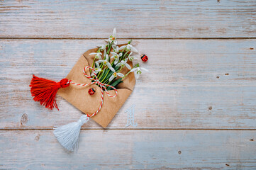 Bouquet of delicate snowdrops in an envelope on a wooden background with Martisor talisman and...