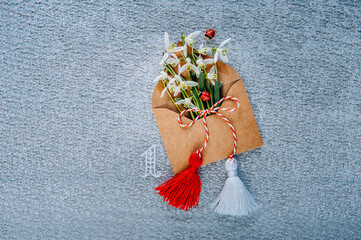 Bouquet of delicate snowdrops in an envelope on ice background with Martisor talisman and number...