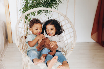 dark-skinned mulattoes A boy and a girl sit in a wicker hanging chair and ride. Children love each...